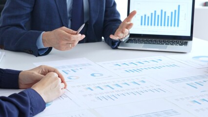 Business people reviewing financial charts and reports in office, using a laptop and calculator while engaging in discussions about strategy and performance