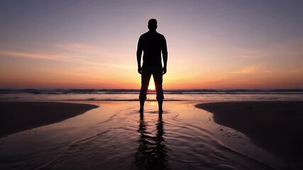 Man silhouette standing strong on beach admiring beautiful sunset reflecting on the water