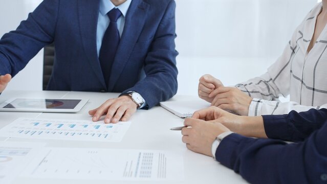 Business people engaging in a corporate meeting, discussing strategies while analyzing financial charts and graphs on a digital tablet alongside printed documents in office - Powered by Adobe
