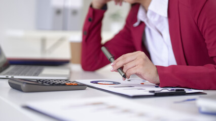 Adult Asian professional reviews financial data business reports with pen calculator laptop at modern office desk workplace