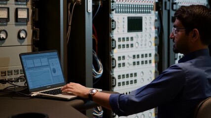 A tech specialist analyzing data on a laptop in a server room. This photo depicts someone focused on technology, monitoring data servers Stock Video - Powered by Adobe