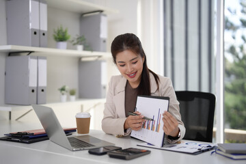 Asian adult businesswoman analyzes financial report in modern office environment pointing out market insights using laptop for strategic planning and growth