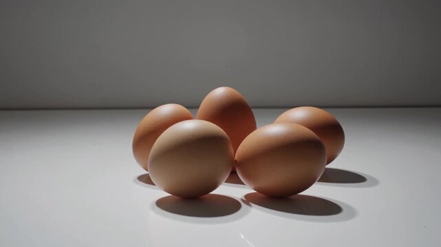Five brown eggs arranged on a smooth white surface in natural light showcasing their texture and shape