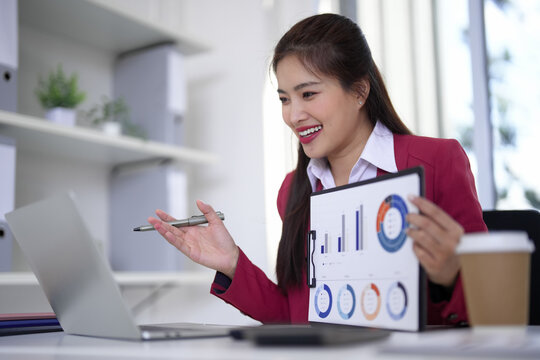 Asian business professional presents financial data online meeting uses laptop computer modern office setting successful women analyzes report performance