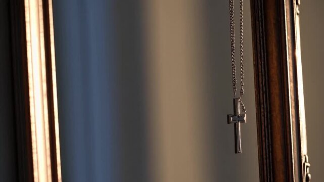 Silver cross necklace hanging in reflective frame during soft afternoon light indoors