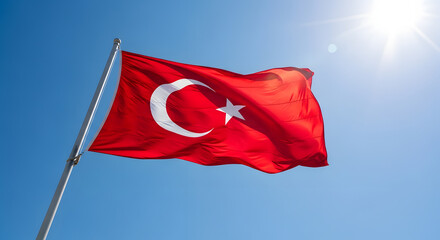 A vibrant turkish flag waving against a clear blue sky with the sun shining brightly above it all