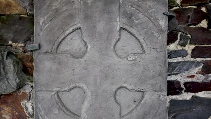 Ancient Manx cross stone tablet with carved circular motifs set against a stone wall.
