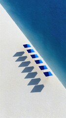 Top Down View Of A Row Of Bright Blue Sun Umbrellas Casting Long Shadows On A White Pebble Beach Next To The Sparkling Blue Ocean On A Sunny Day