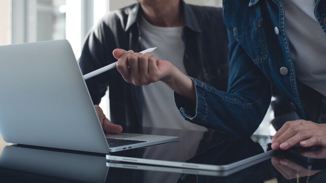 Coworking team brainstorming in modern office. Asian business project team working together at meeting room, having a discussion and analyzing sales data on laptop computer