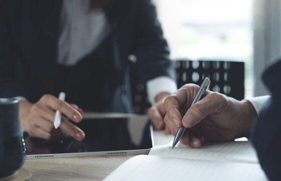 Business colleague working together at office, close up. Business colleague using tablet, having a discussion during meeting and writing on notebook, business planning and solution concept - Powered by Adobe