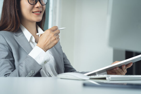 Asian business woman working, having a video conference via desktop computer with colleagues and using digital tablet in office. Smiling businesswoman online meeting, web conference, close up - Powered by Adobe