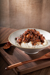 A close-up of a bowl of Taiwanese braised pork rice against a retro linen and wooden background.