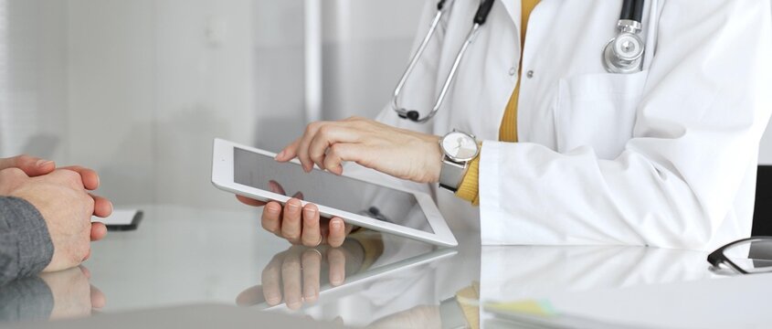 Doctor consulting patient using digital tablet, explaining medical information during modern healthcare appointment. Medicine, healthcare and science concept