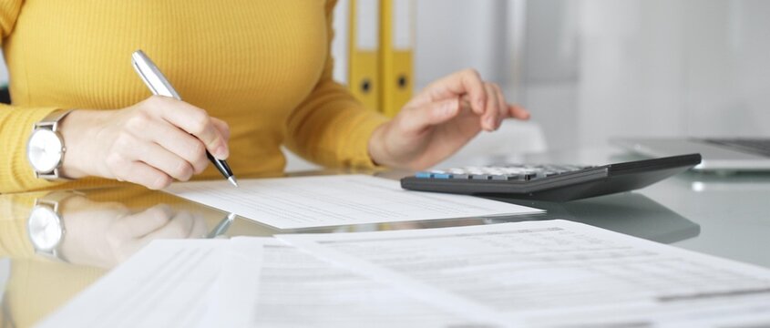 Woman calculating finance, taxes, and accounting paperwork at office desk, budgeting expenses, filing documents. Audit and taxes in business