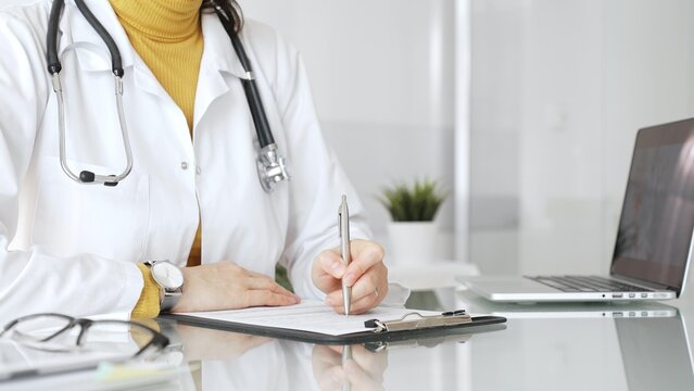 Female physician or medic completing paperwork, preparing a diagnosis, or providing healthcare service in a clean modern office. Medicine, healthcare and science concept