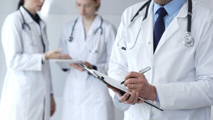 During a discussion with the medical team, a physician takes notes on a clipboard, capturing aspects of collaborative patient care, documentation, and clinical healthcare strategies