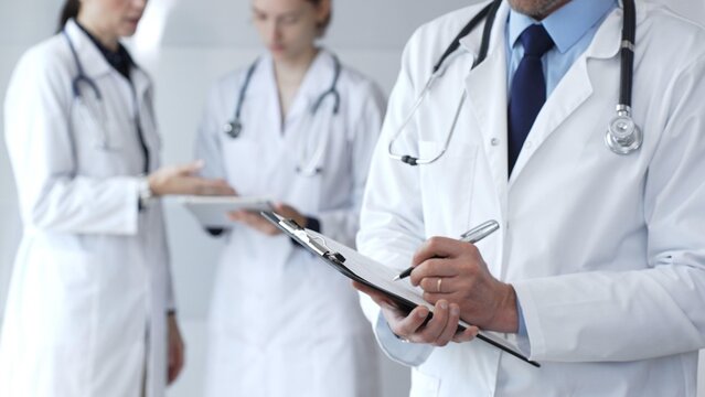 During a discussion with the medical team, a physician takes notes on a clipboard, capturing aspects of collaborative patient care, documentation, and clinical healthcare strategies
