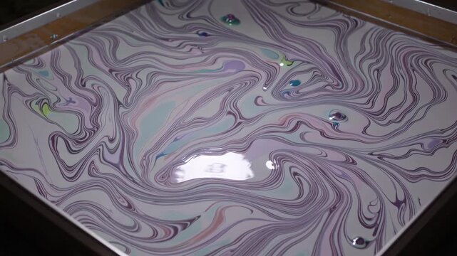 Swirling inks with reflective surface, Ornamental marbling display with floating droplets, Studio capture highlighting intricate textures and hypnotic movements in pastel marbling water