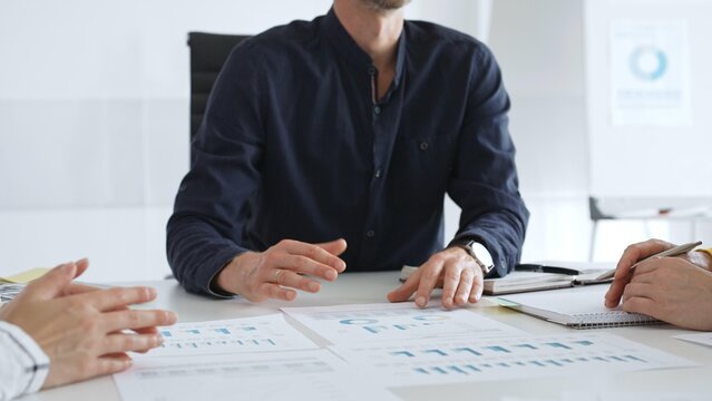 Business people team analyzing financial data and discussing growth strategy during meeting, pointing at charts and graphs, taking notes in modern office
