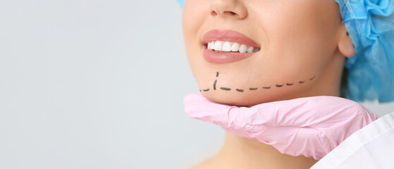 Plastic surgeon touching face of young woman on light background, closeup