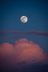Full moon over pink clouds against a dark blue evening sky provides a serene view