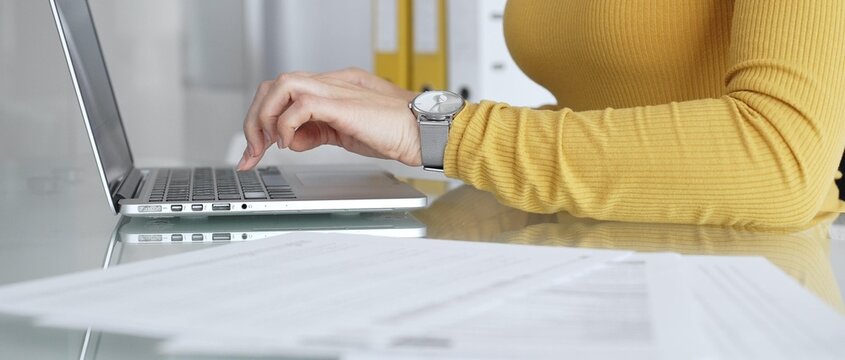 Woman working on laptop, typing on keyboard in office, managing business documents on desk, focusing on digital marketing communication and online data entry