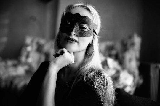 Mysterious woman wearing a black mask is seated on a cozy bean bag chair, surrounded by soft textures and natural light, creating an intimate and enigmatic atmosphere