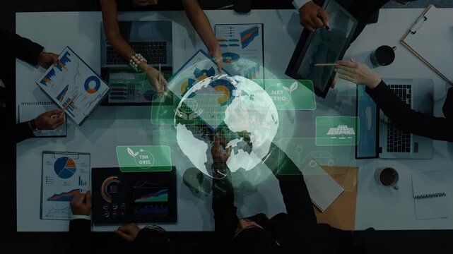 Aerial view of a business team engaged in a strategic meeting focused on sustainability and planning. Digital globe overlay emphasizes global impact and responsibility. Raster