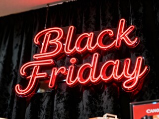A bright red neon sign that says black friday hangs in front of a dark curtain