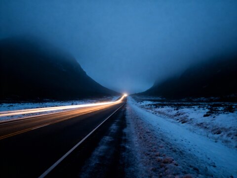 Long exposure of car light trails on a snowy road at dusk with mountains in the background