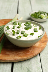 Bowl of tasty sour cream with green onion on light wooden background