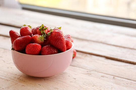 Bowl with fresh strawberries on white wooden table