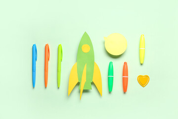 Paper rocket with different stationery and speech bubble on green background