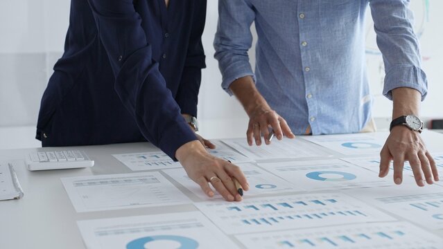 Professional team reviewing financial documents, pointing at charts on desk, collaborating to analyze data and strategize business growth. Business people concept