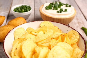 Bowls of tasty sour cream with sliced green onion and potato chips on grey wooden background