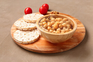 Bowl of fresh chickpeas covered with plastic food wrap and rice crackers on brown background
