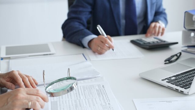 Two professional chartered accountants reviewing financial reports and analyzing data using a calculator and a magnifying glass, ensuring accuracy and compliance. Audit and taxes in business - Powered by Adobe