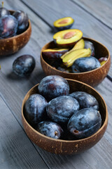 Bowls with fresh plums on blue wooden background