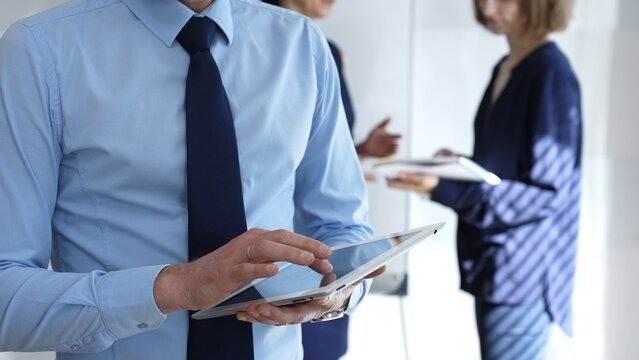 Businessman hands holding and using a digital tablet for work, navigating information and checking data during a modern corporate meeting