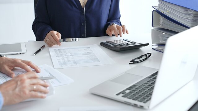 Business team of business man and female entrepreneur analyzing financial documents, using calculators and laptop, working together on project in modern office. Audit and taxes concept - Powered by Adobe