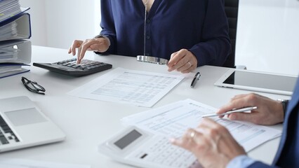 Business team of male and female accountants analyzing financial documents, using calculators and laptop, working together on project in modern office. Audit and taxes concept