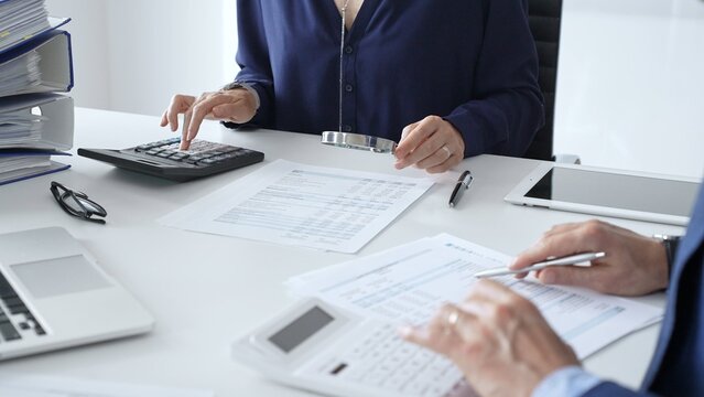 Business team of male and female accountants analyzing financial documents, using calculators and laptop, working together on project in modern office. Audit and taxes concept