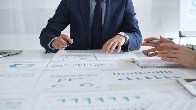 Business professionals discussing financial reports and marketing charts during corporate meeting, focusing on strategy, planning, data analysis, and teamwork