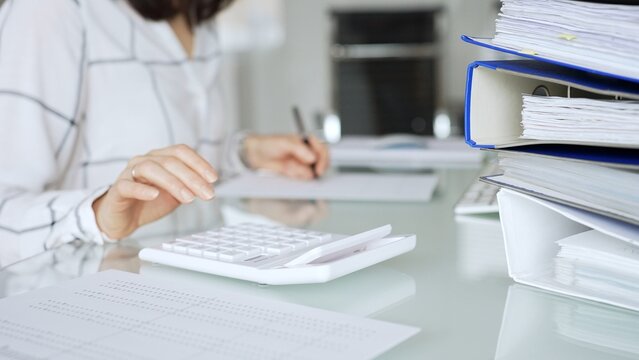 Woman working in office, calculating finances with white calculator, managing accounting paperwork and business expenses. Audit and taxes in business