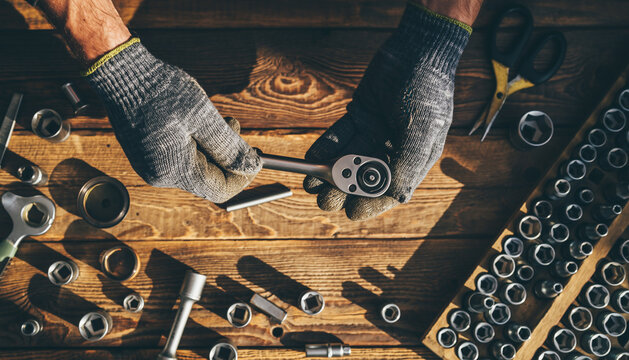 Close-up of a mechanic's gloved hands holding a socket wrench over a wooden workbench with various tools