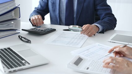 Male financial analysts with female colleague examining documents, using magnifying glass and...