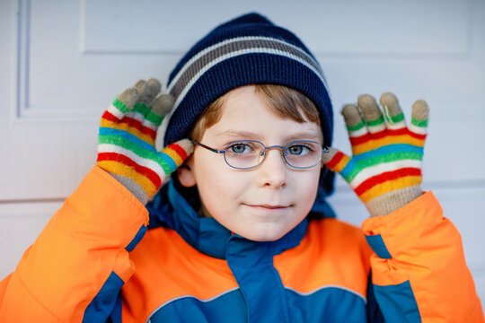 Portrait of little cute school kid boy with glasses and colorful winter fashion clothes. Child smiling and having fun with the camera. Winter, spring or autumn fashion. Kid with missing front teeth