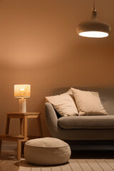 Interior of modern living room with cozy sofa, pouf and glowing lamps
