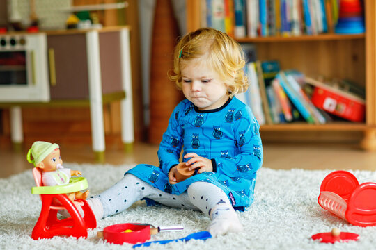 Cute little girl playing with doll. Happy healthy baby child having fun with role game, playing mother at home or nursery. Active toddler with toy.
