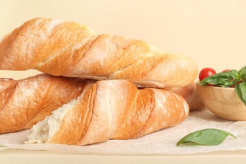 Baking paper with fresh baguettes, basil and cherry tomatoes on beige background